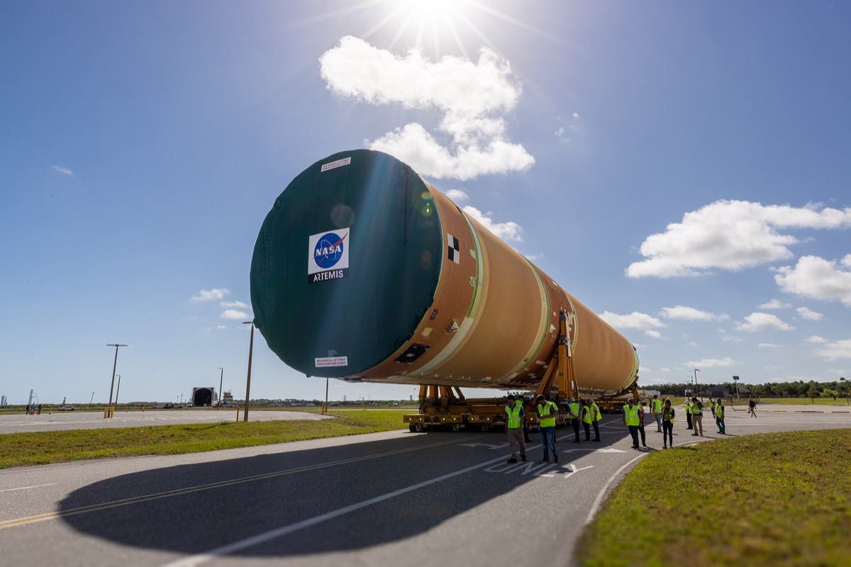 Estágio central do foguete SLS da missão Artemis III sendo transportado sobre plataforma rodante, com equipe ao lado
