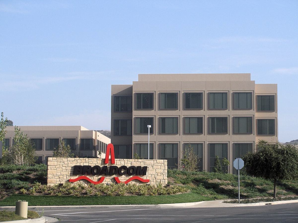 Fachada de vidro da sede corporativa da Broadcom, com jardim e placa da empresa.