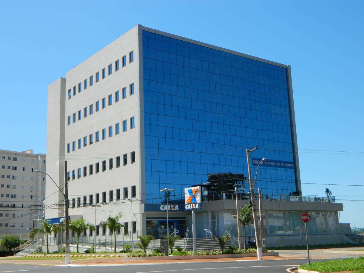 Fachada de vidro e concreto do edifício da sede administrativa da Caixa Econômica Federal, com o letreiro do banco no alto da construção