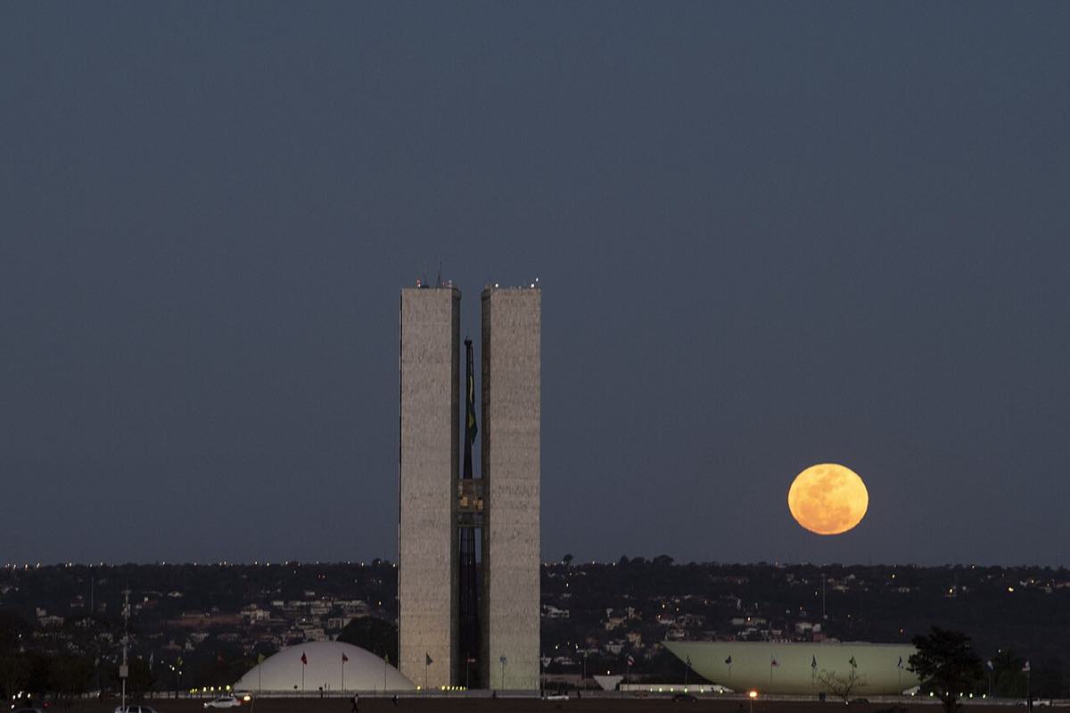 As torres do Congresso Nacional em Brasília no fim da tarde, com a lua cheia alaranjada subindo à direita
