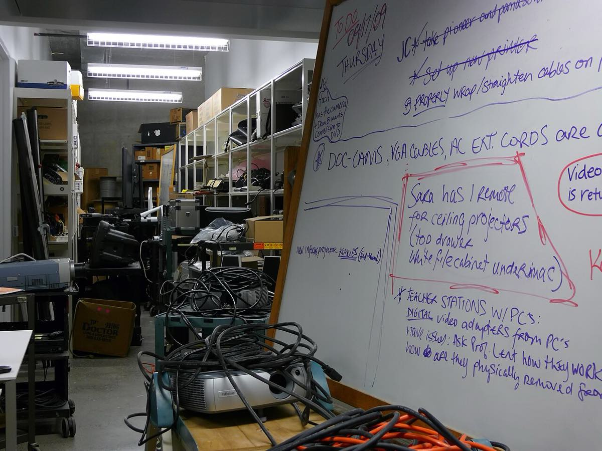 Depósito com prateleiras de equipamento audiovisual e de informática, cabos enrolados e projetores