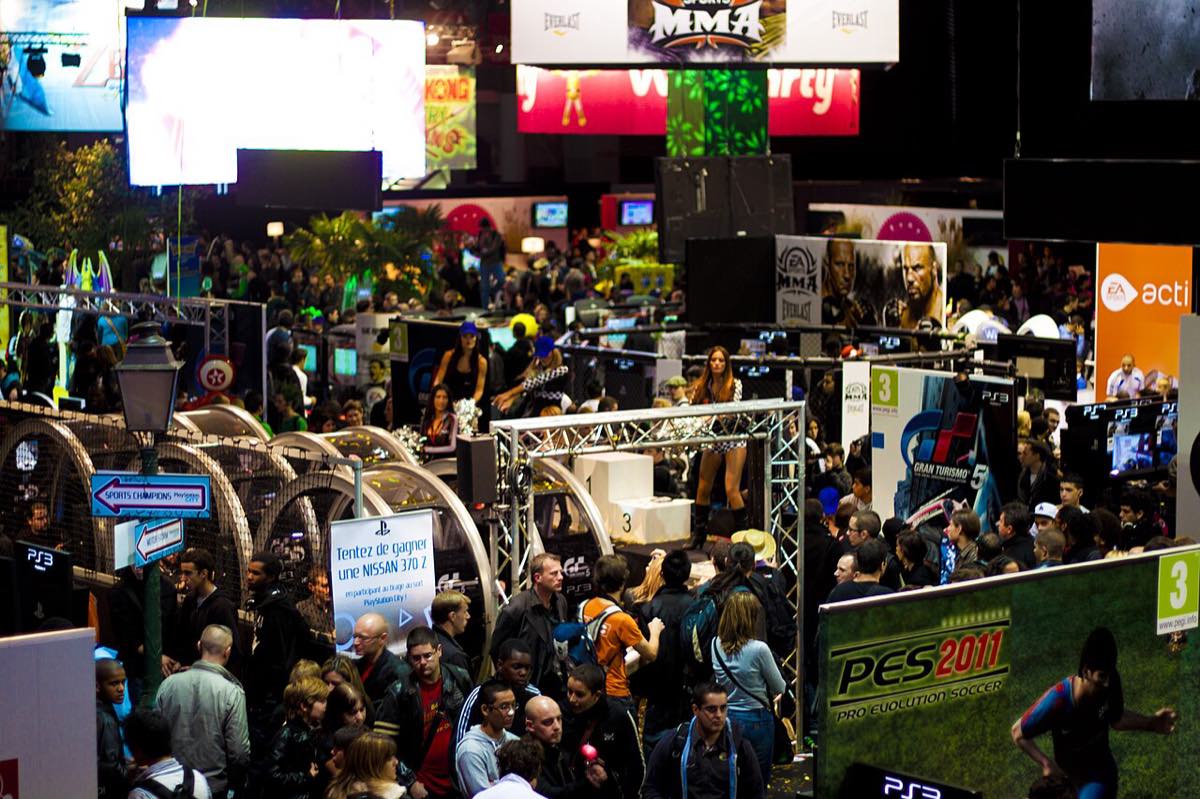 Vista geral do salão da Paris Games Week, feira francesa de videogames, com estandes e público circulando.