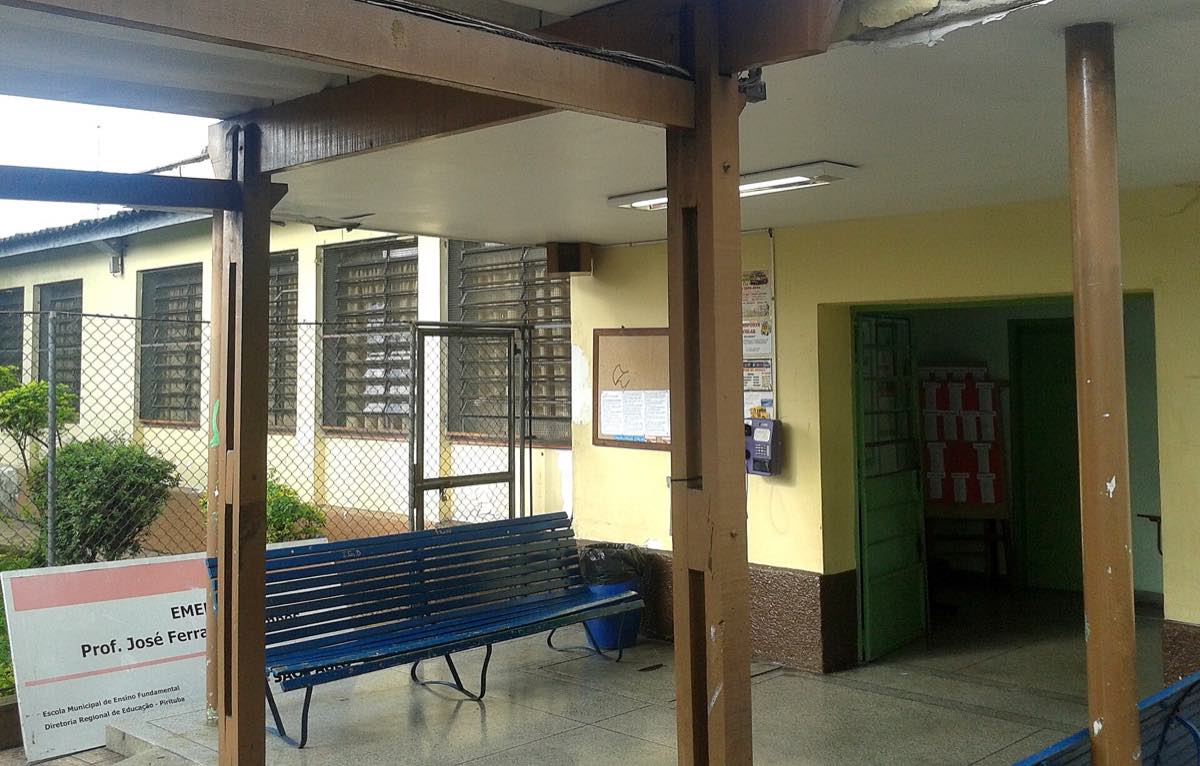 Fachada de escola municipal de São Paulo, prédio baixo com muro pintado e portão, vista da calçada em dia claro