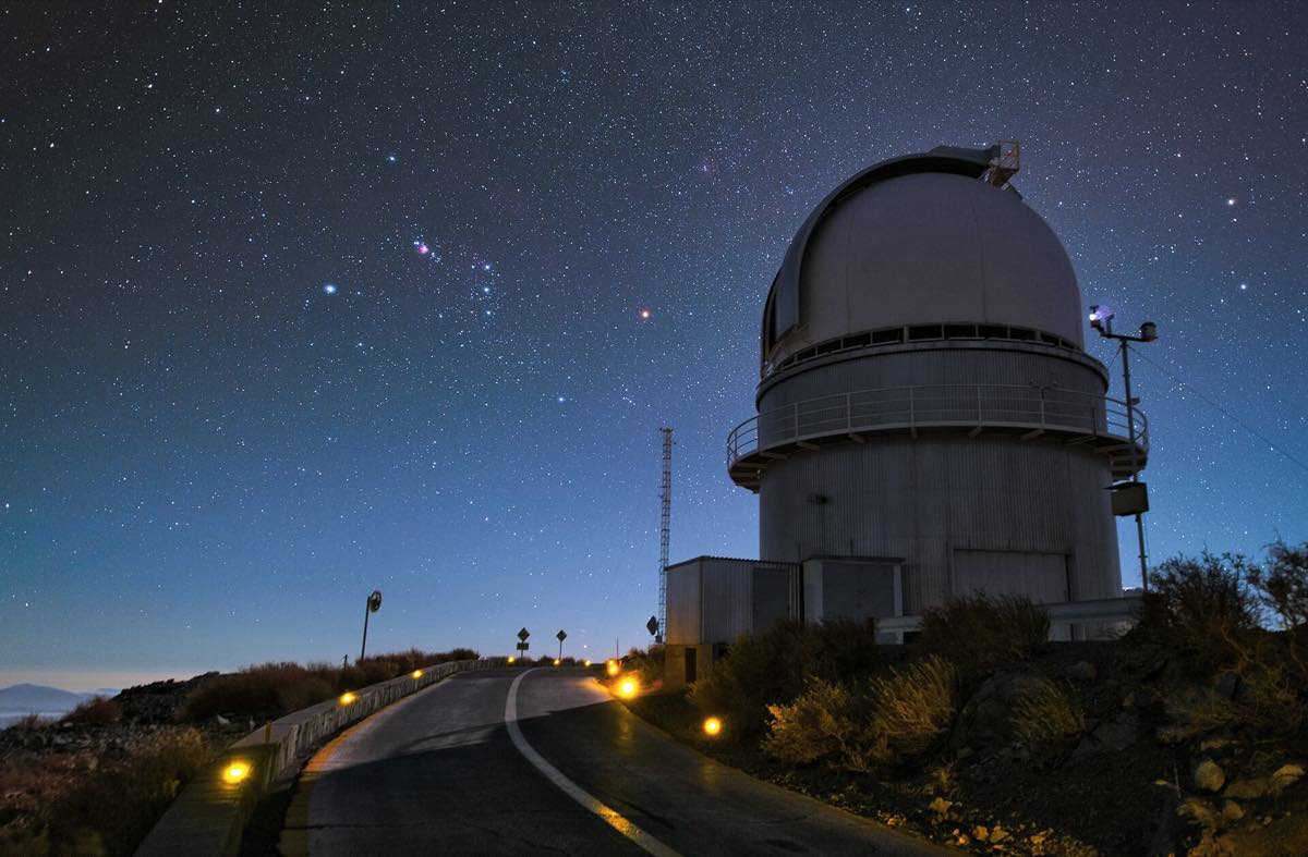 Cúpula do telescópio de 3,6 metros do ESO aberta à noite no Observatório de La Silla, no deserto chileno, com o céu estrelado ao fundo e a estrutura iluminada por luz fraca