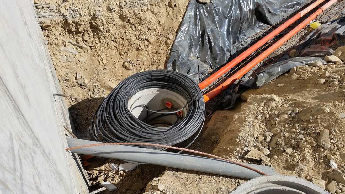 Rolo de cabo de fibra óptica e dutos laranja dentro de uma vala aberta em obra