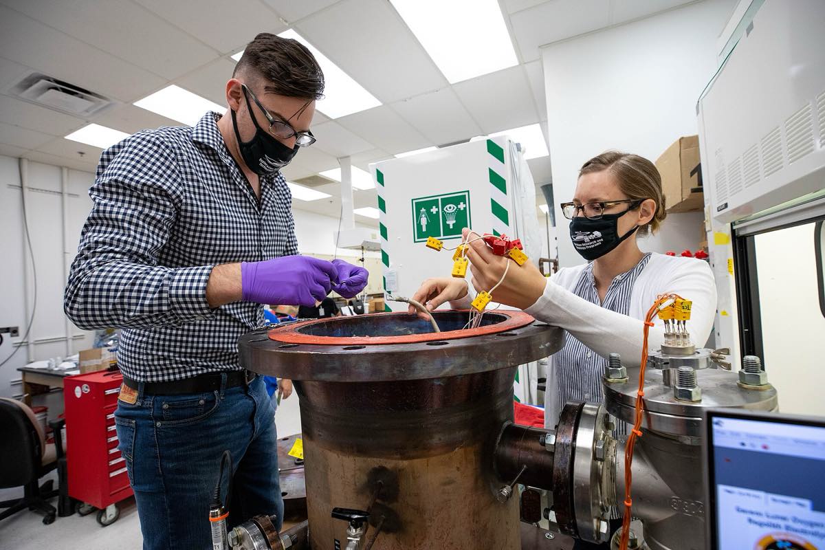 Dois pesquisadores de jaleco e máscara conferem equipamento de laboratório usado para derreter simulante de regolito lunar, no Centro Espacial Kennedy