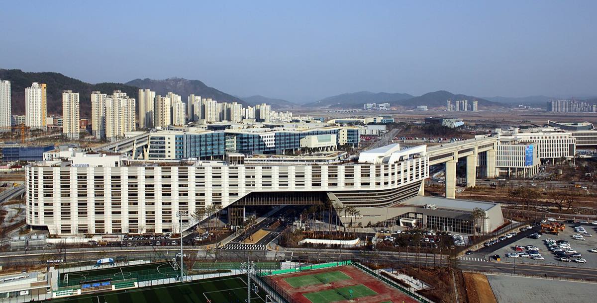 Vista noturna do Complexo Governamental de Sejong, sede de ministérios da Coreia do Sul, com blocos iluminados e um longo terraço curvo.