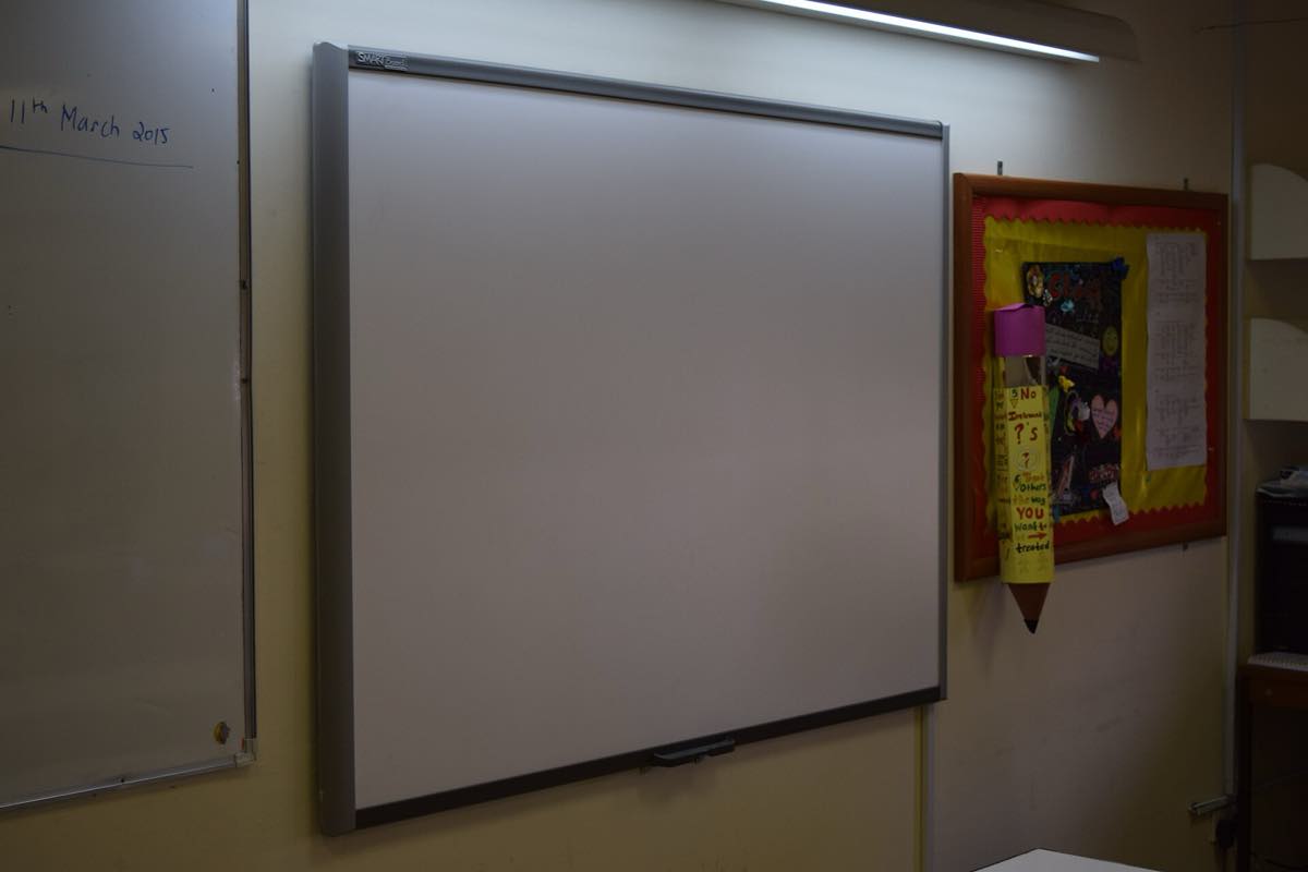 Lousa digital interativa instalada na parede de uma sala de aula, ao lado de um quadro branco comum