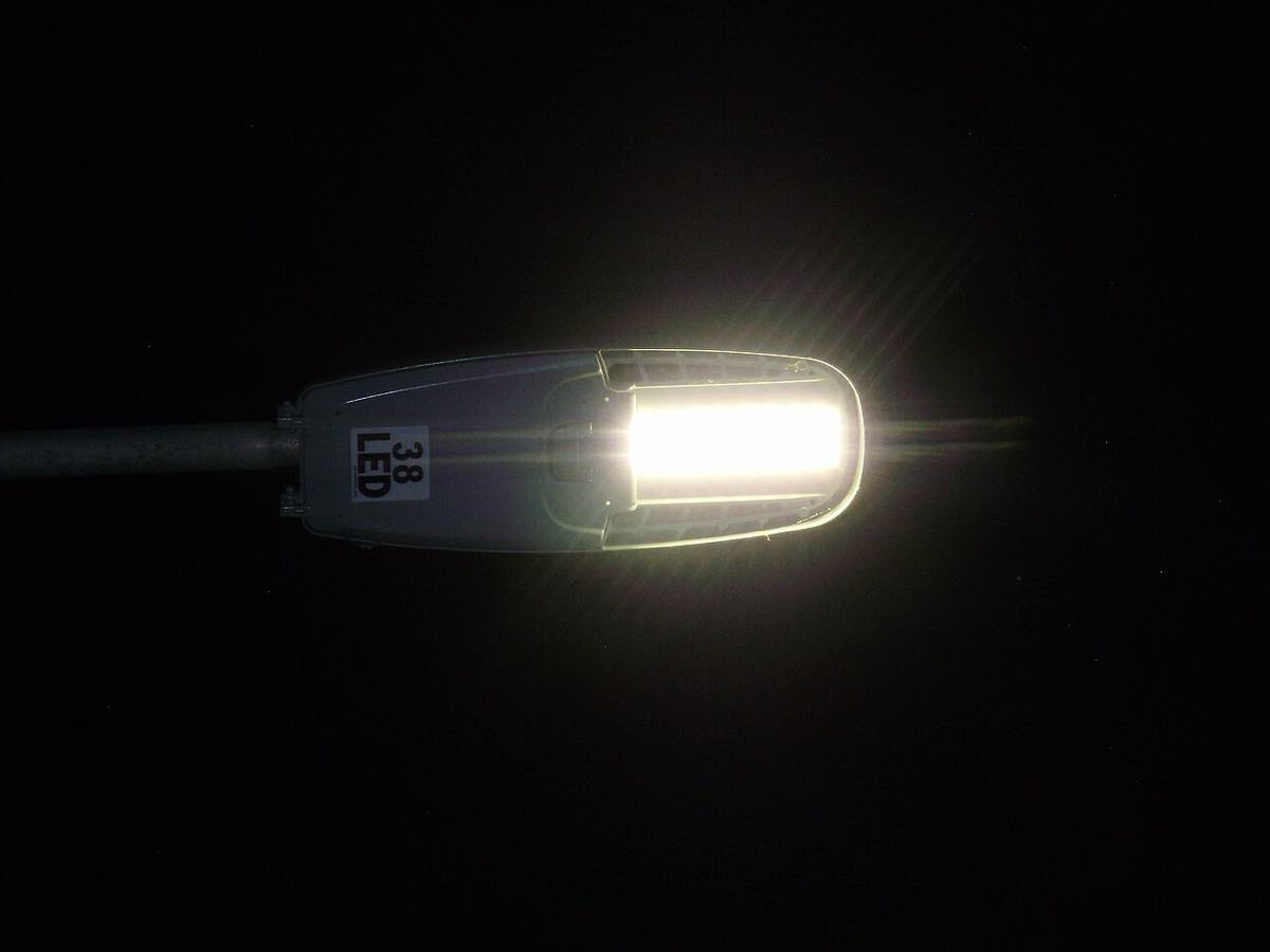 Luminária de LED acesa no alto de um poste, à noite, contra o céu escuro