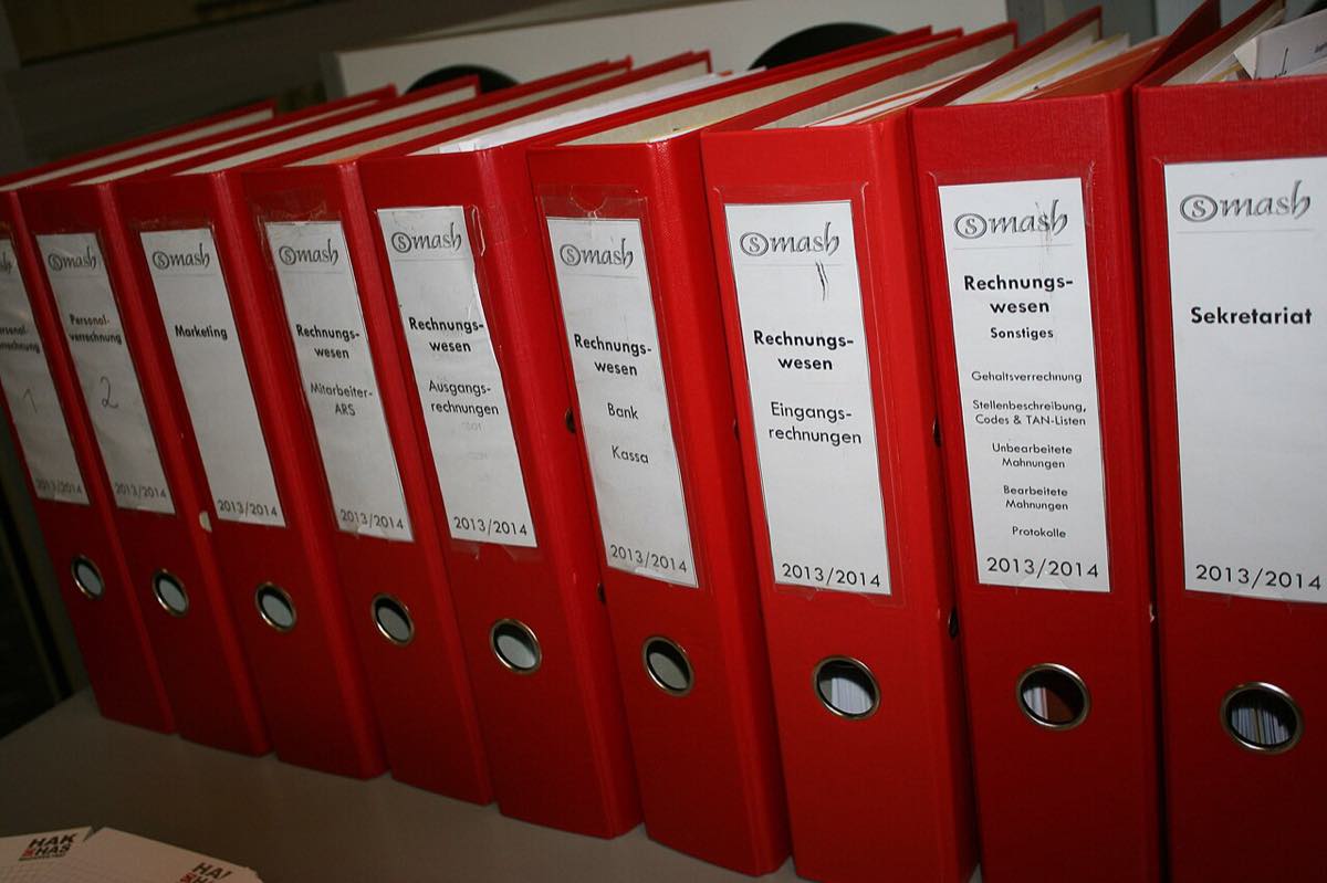 Fileira de pastas de arquivo vermelhas com etiquetas, vistas de lado numa prateleira de escritório