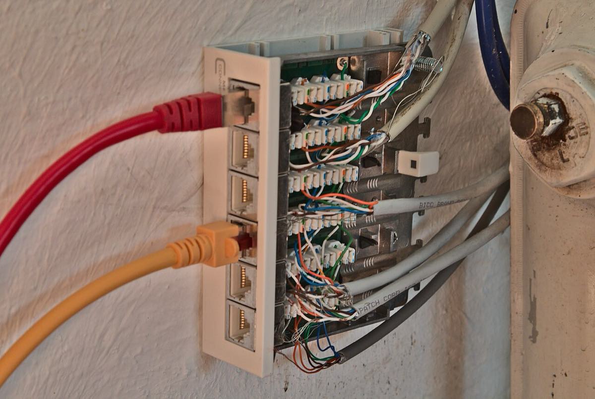 Painel de conexão de rede montado em parede, com portas Ethernet e cabos organizados