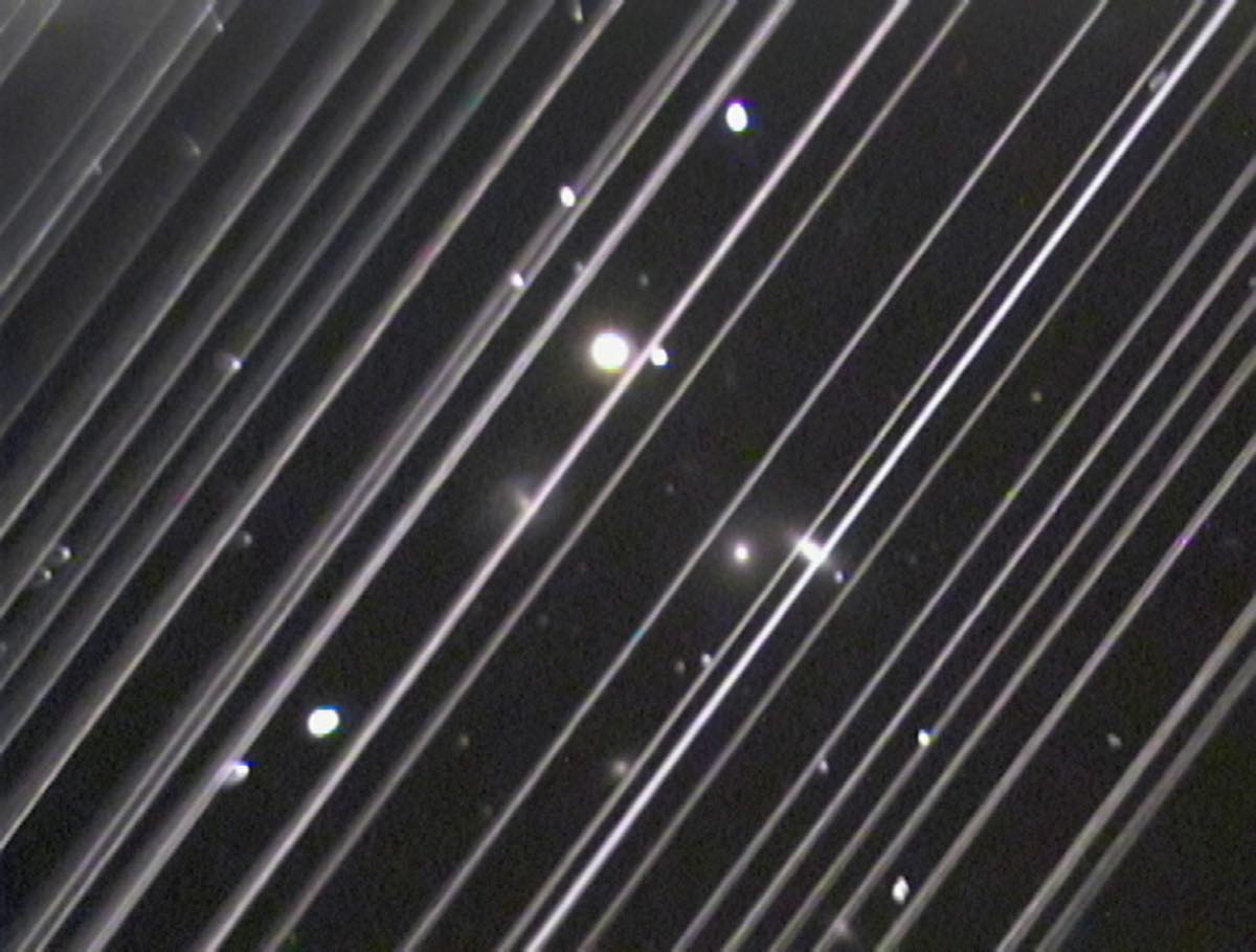 Imagem astronômica riscada por dezenas de faixas brancas paralelas deixadas por satélites Starlink atravessando o campo do telescópio
