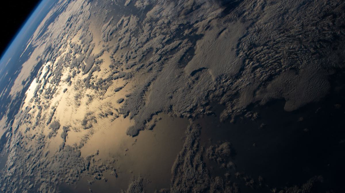 Fotografia tirada da Estação Espacial Internacional mostrando o reflexo prateado do Sol sobre o oceano Índico, com a curvatura da Terra e o horizonte azul ao fundo