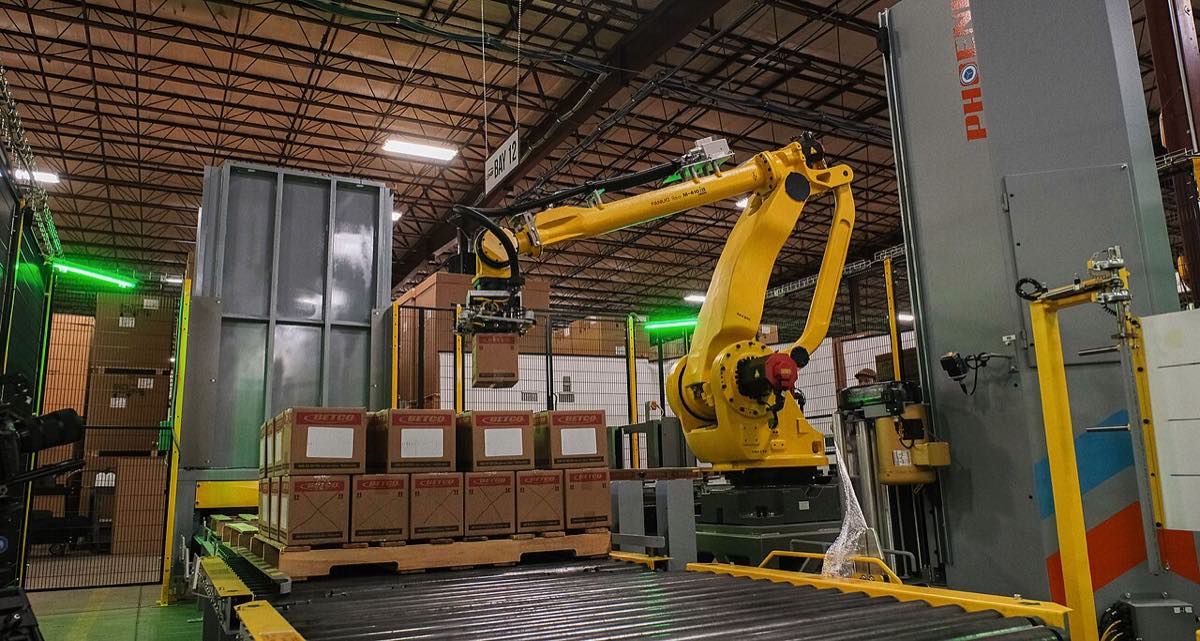 Braço robótico industrial empilhando caixas sobre um palete em uma fábrica