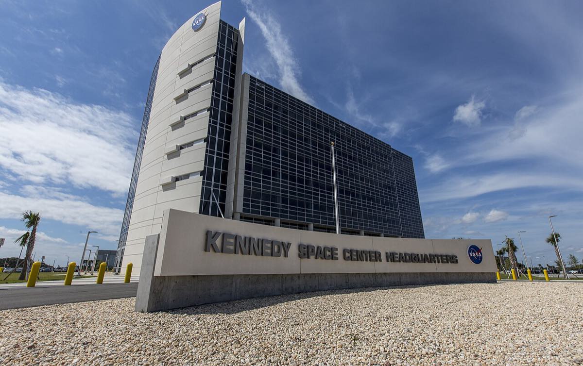 Fachada do prédio-sede do Centro Espacial Kennedy, na Flórida, com o letreiro Kennedy Space Center Headquarters e o logotipo da NASA em primeiro plano