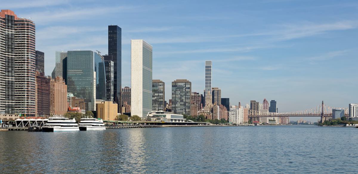 Sede das Nações Unidas vista da margem do East River, em Nova York, com o edifício da Assembleia Geral e a torre do Secretariado alinhados à beira d'água sob céu claro