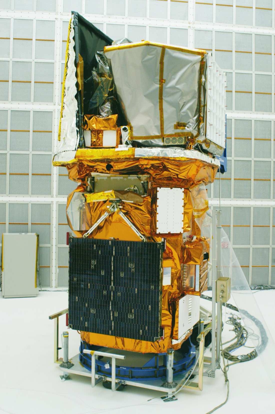 O satélite Swift, envolto em manta térmica dourada e com painéis solares recolhidos, sobre uma plataforma de montagem dentro de um hangar em Cabo Canaveral.