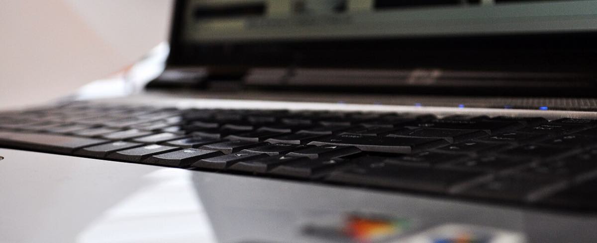 Close lateral do teclado de um notebook aberto, com a tela desfocada ao fundo