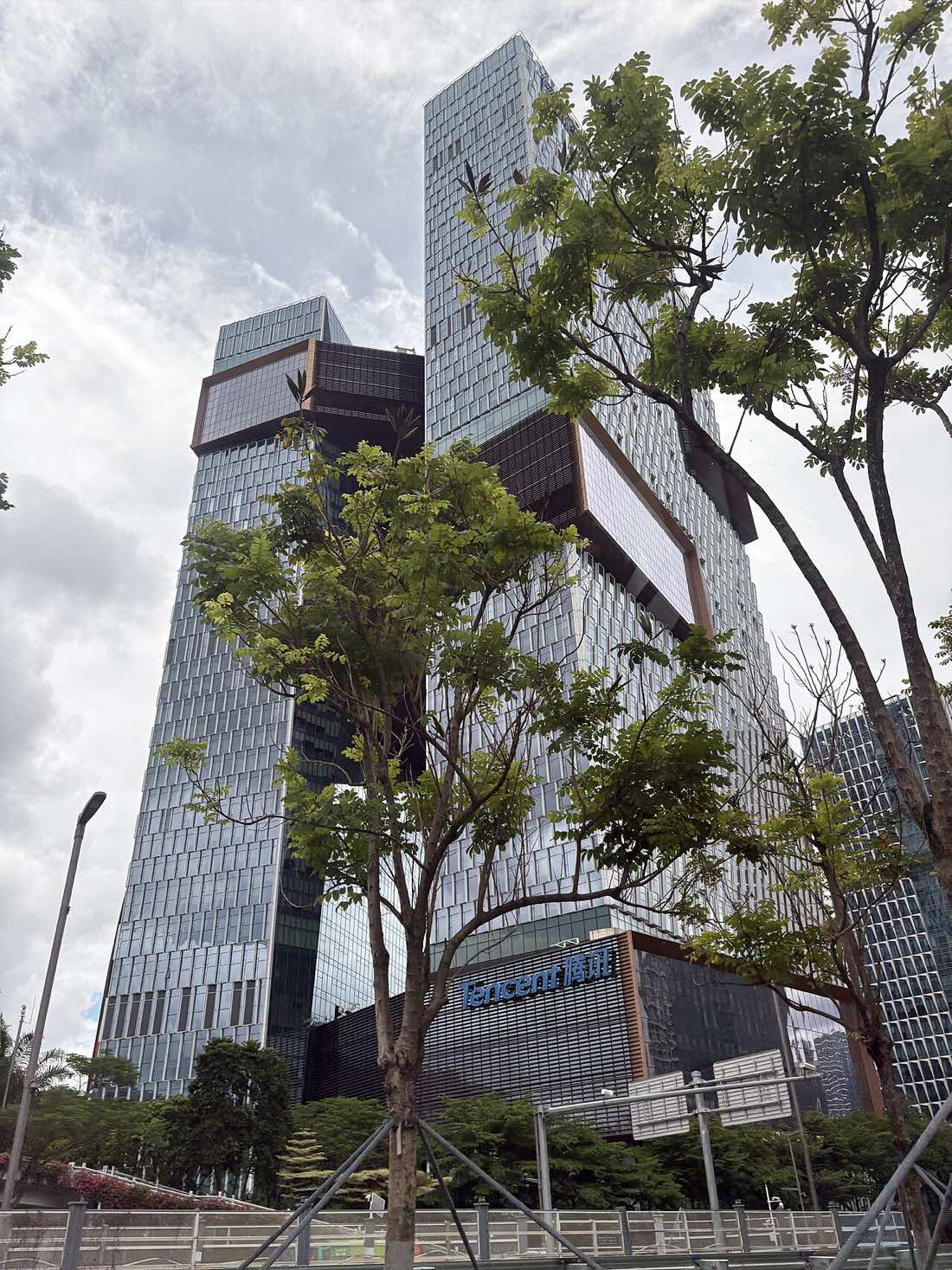 As torres da sede da Tencent em Shenzhen, dois arranha-céus de vidro ligados por passarelas elevadas, vistos de baixo.