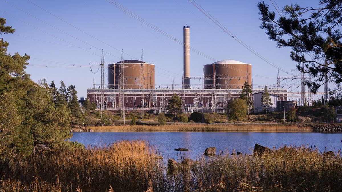 A usina nuclear de Loviisa, na Finlândia, vista da água: prédios industriais claros junto ao mar, com guindaste e linhas de transmissão