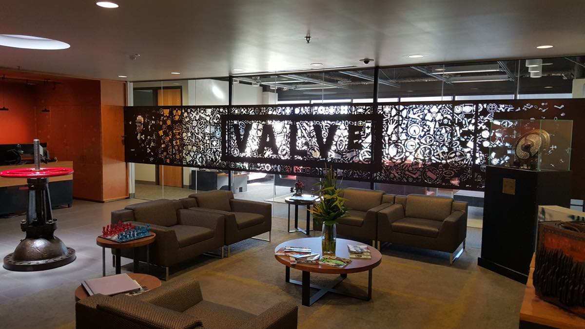 Saguão de entrada dos escritórios da Valve em Bellevue, Washington, em 2016, com sofás, mesa de sinuca ao fundo e uma divisória de metal vazado com o nome da empresa