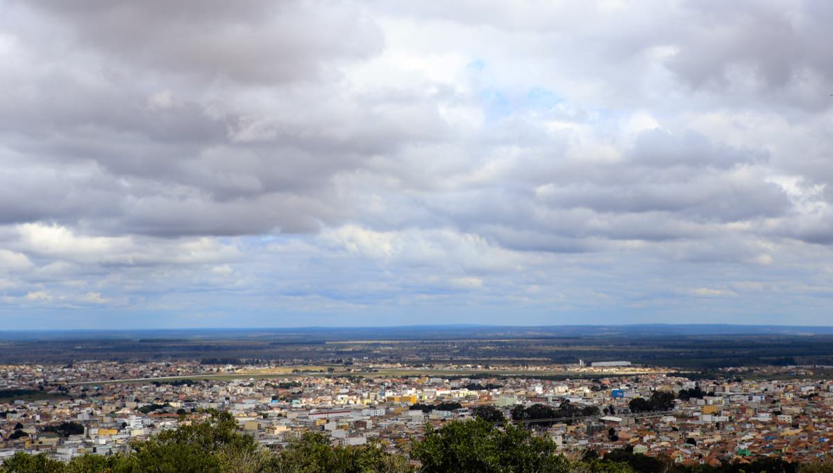 Vista da cidade de Vitória da Conquista, na Bahia, com prédios e vegetação sob céu com nuvens