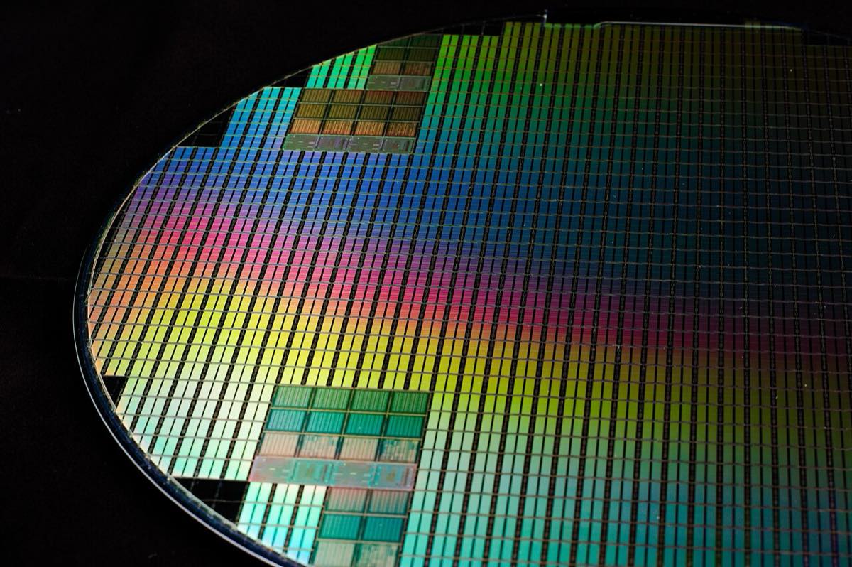 Um wafer de silício circular, com reflexos coloridos, exibindo dezenas de chips.