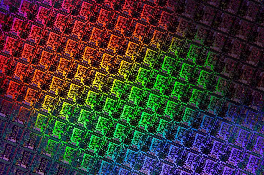 Wafer de silício circular refletindo cores iridescentes de azul, violeta e laranja.